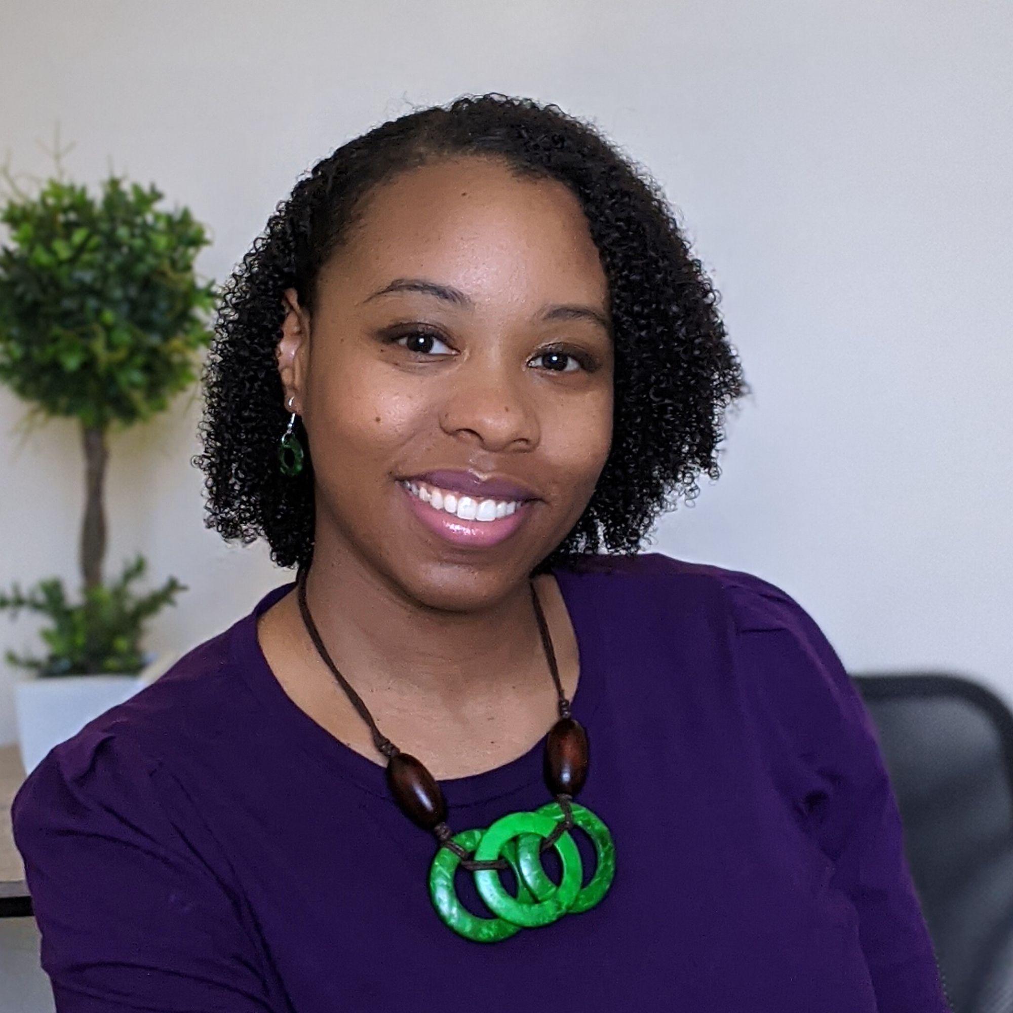 SEO Geneva Bell wearing a purple shirt and green necklace.